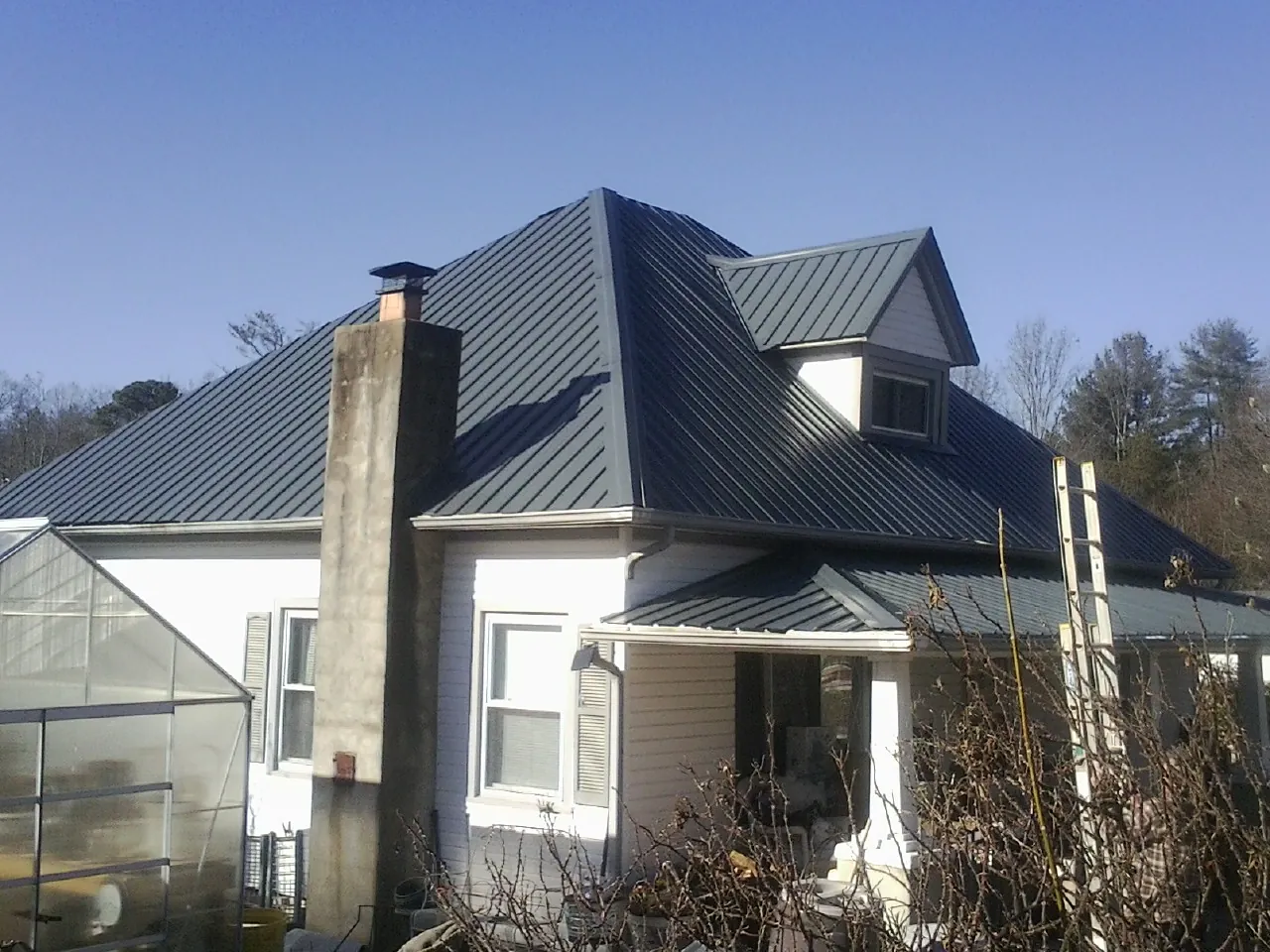Dark blue standing seam metal roof on a white farmhouse with dormer — Slate & Tile Roof Repair by Roofing Brothers in Shreve