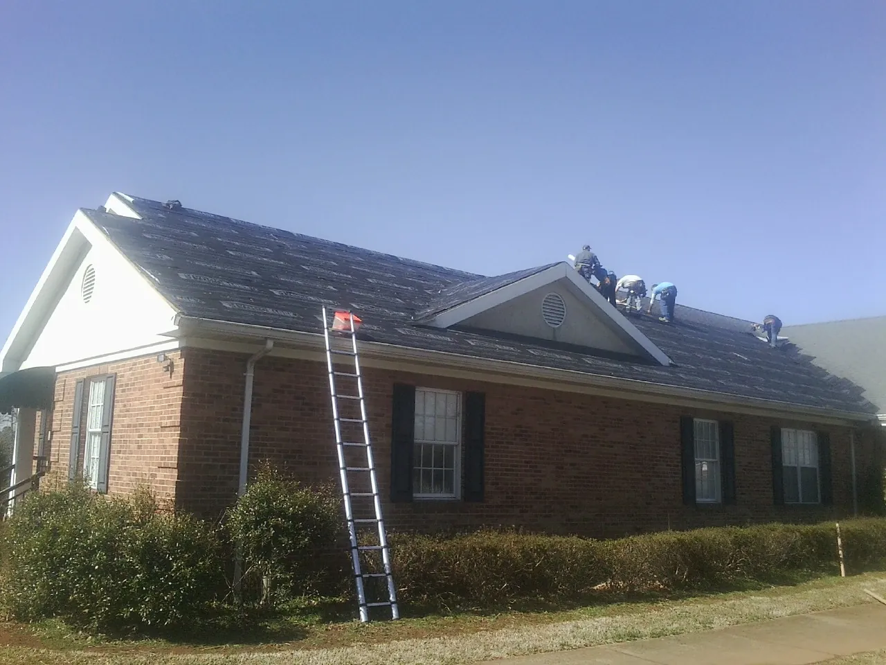 Crew tearing shingles off a brick ranch roof with a ladder set — Metal Roof Repair work by our crew in Shreve