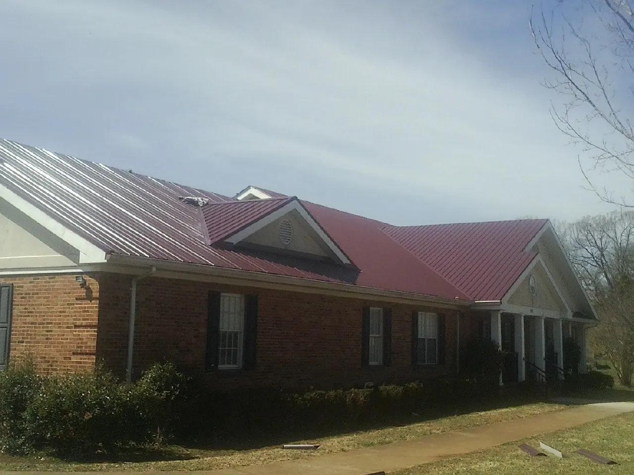 Red metal roof with gabled entries on a long brick building, from a Hail Damage Roof Repair job in Shreve