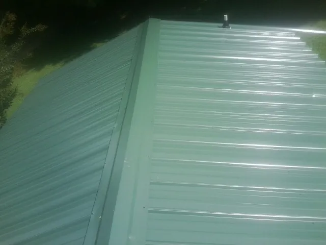 New green metal panels meeting at the ridge of a roof — Flat Roof Repair work by our crew in Shreve