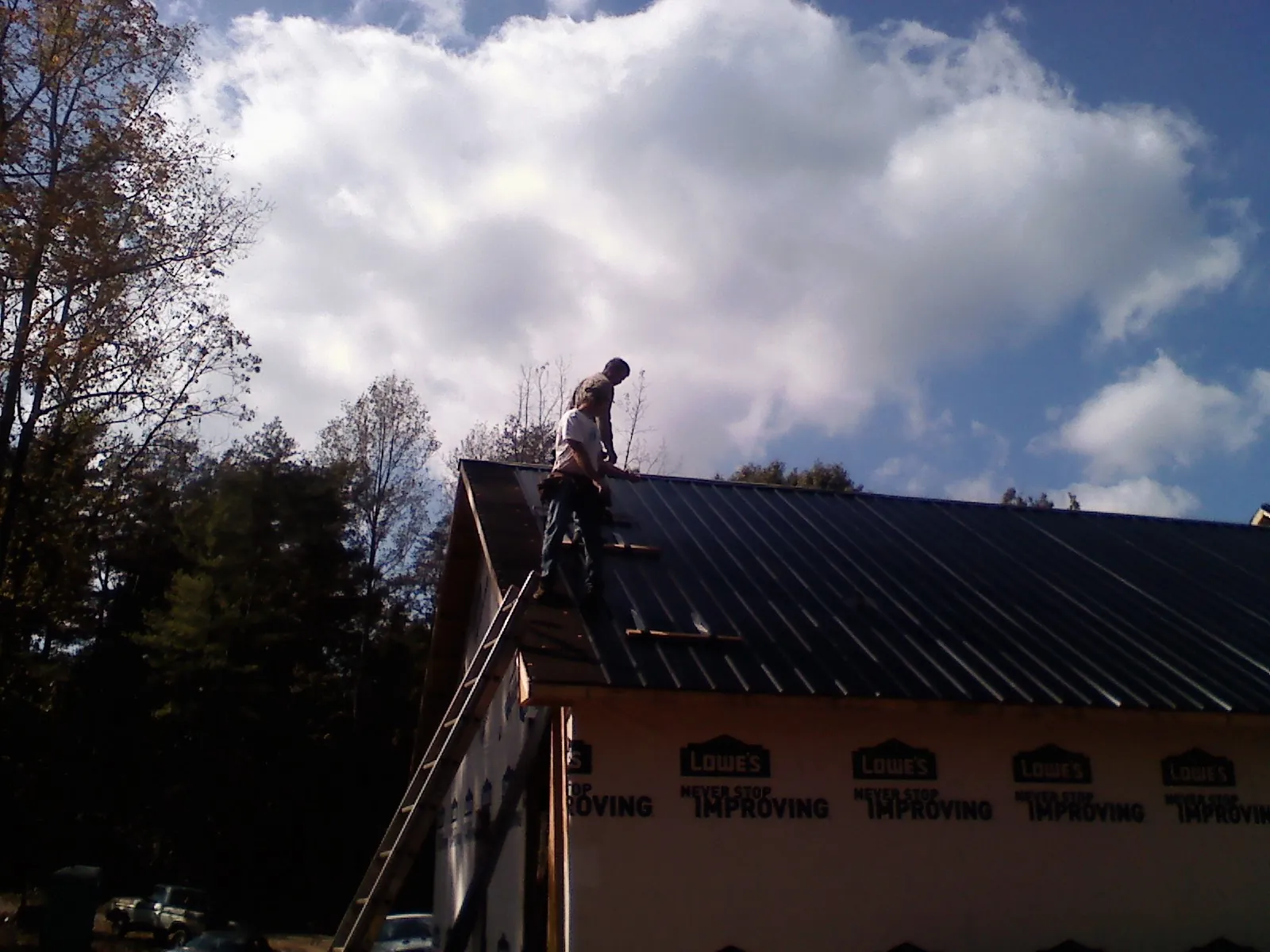 Roofer fastening dark metal panels high against a cloudy sky, from a Roof Inspection job in Shreve