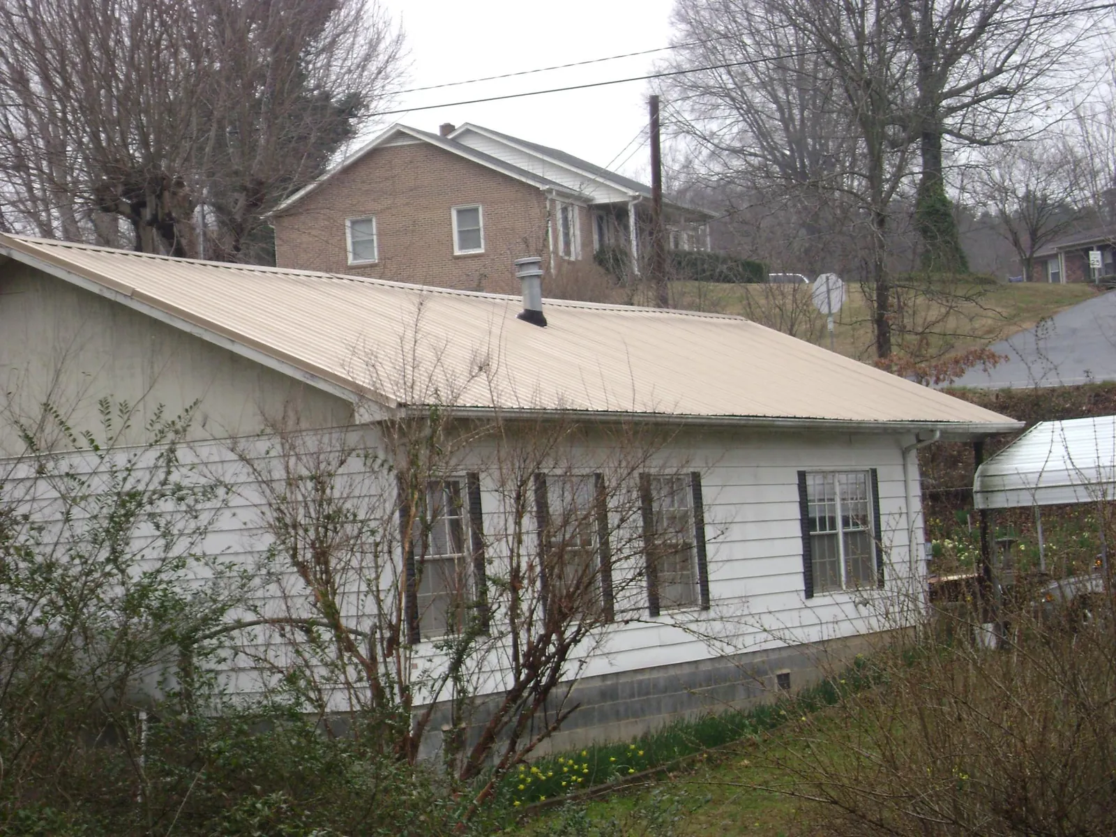 Tan metal roof on a white sided house set into a hillside — Commercial Roofing by Roofing Brothers in Shreve