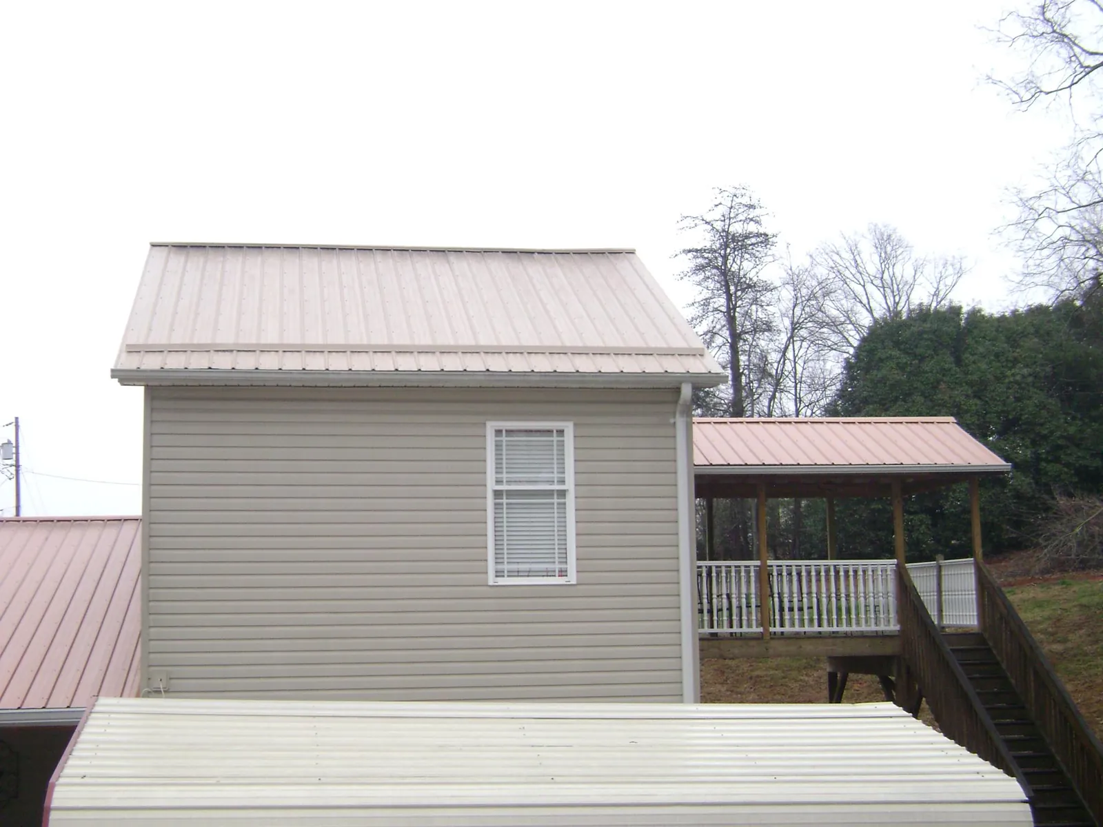 Tan metal roofs on a two story addition and attached porch, from a Roof Replacement job in Shreve
